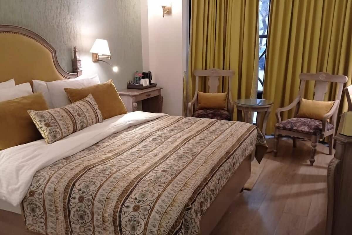 Une chambre d’hôtel avec un grand lit, deux chaises, une petite table et une fenêtre avec des rideaux.