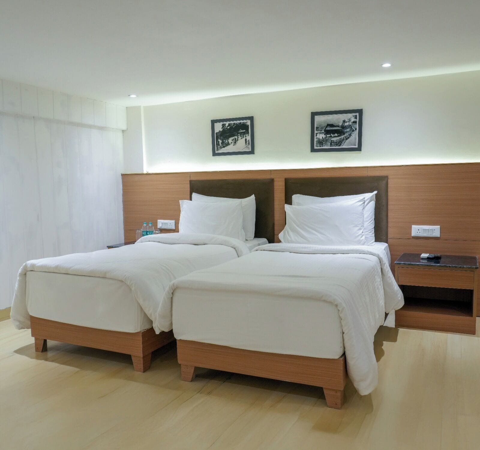 A double bed with a wooden headboard, two pillows, and a bedside table with a remote control.