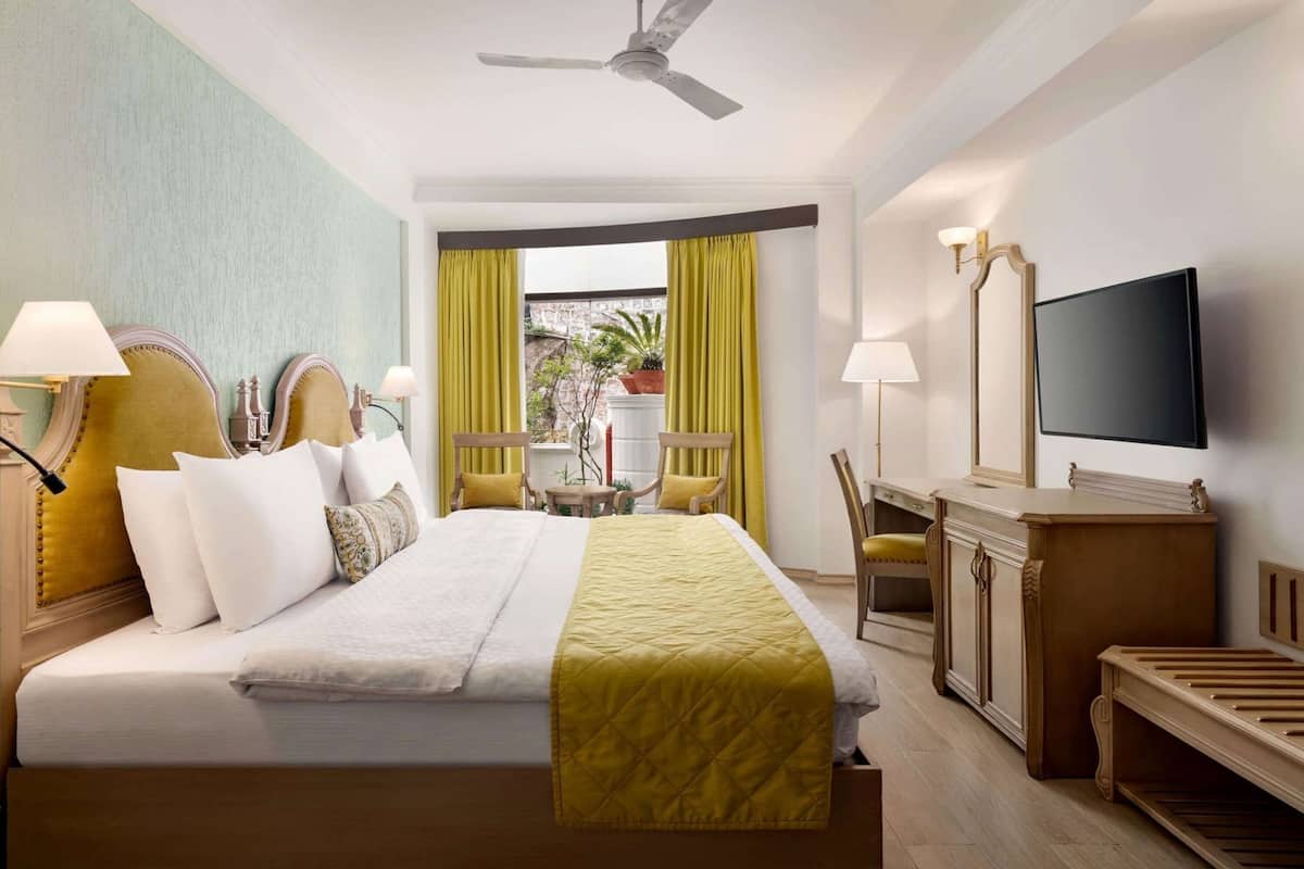 Une chambre d’hôtel équipée d’un lit, d’un bureau, d’une chaise, d’une télévision et d’un ventilateur de plafond.