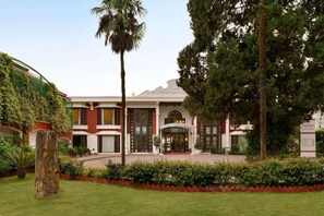 Classic hotel with a symmetrical facade, surrounded by lush greenery and a central entrance.