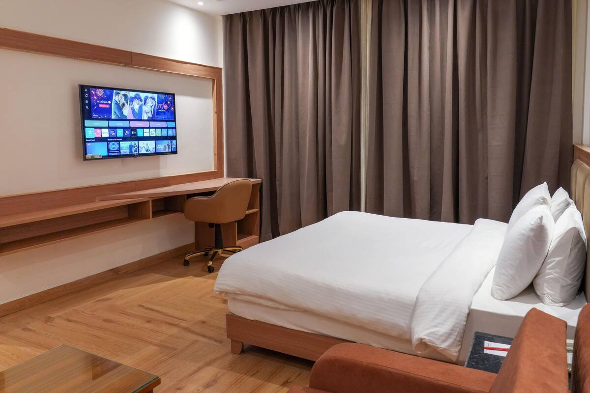 Une chambre d’hôtel équipée d’un lit, d’un bureau, d’une chaise, d’une télévision et d’une fenêtre avec des rideaux.