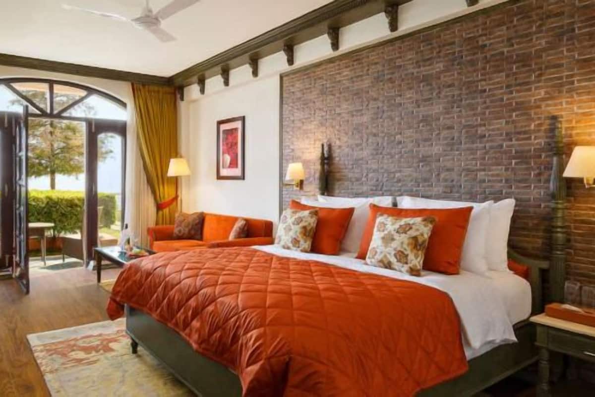 Une chambre d’hôtel avec un grand lit, un bureau, une chaise et un téléviseur. Il y a un mur en briques et une fenêtre avec des rideaux.