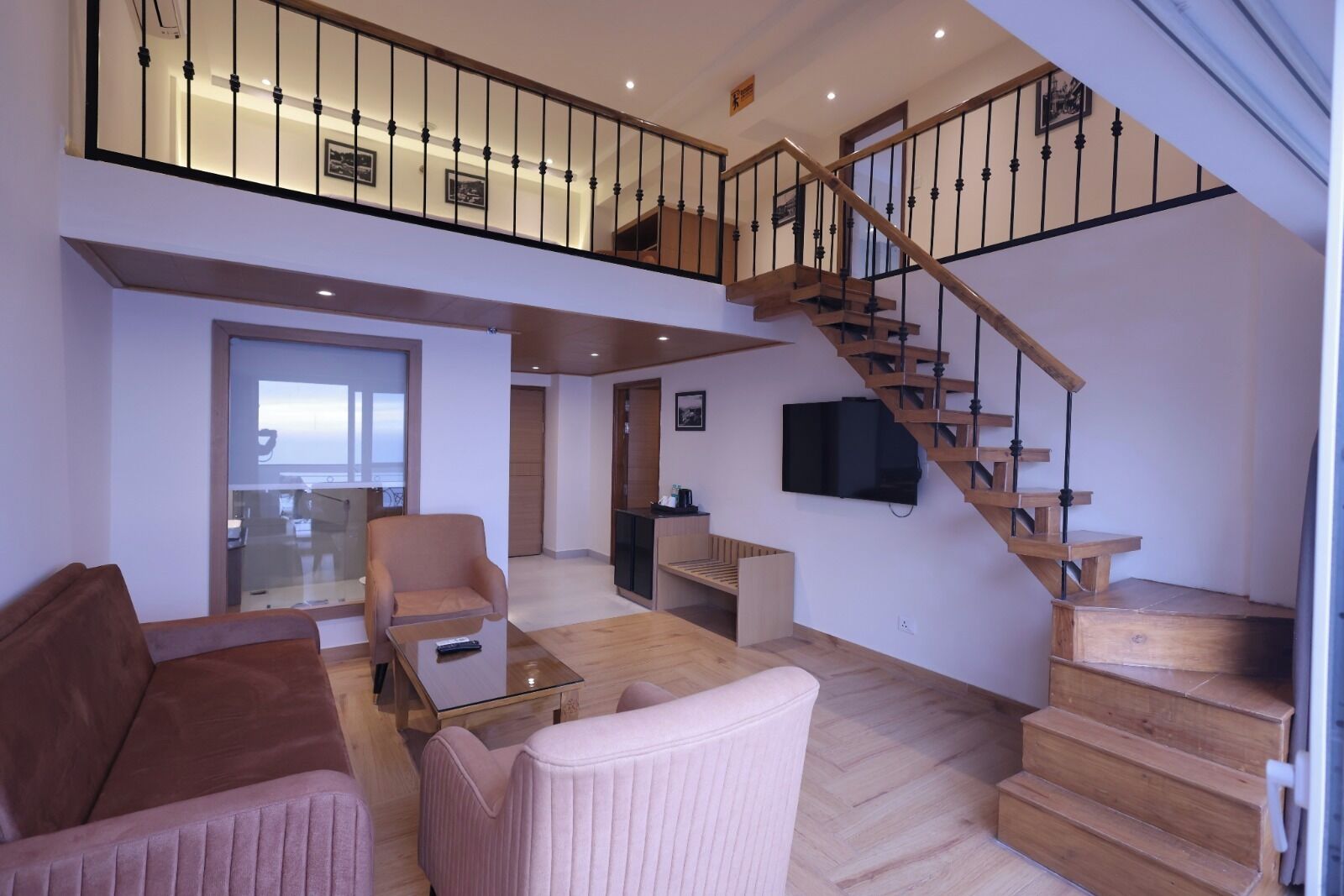 A spacious living area with a high ceiling, a wooden staircase, and a flat-screen TV mounted on the wall.