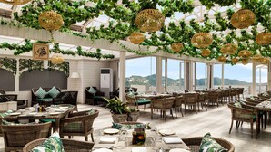A spacious outdoor dining area with wicker furniture, green cushions, and hanging wicker lamps.