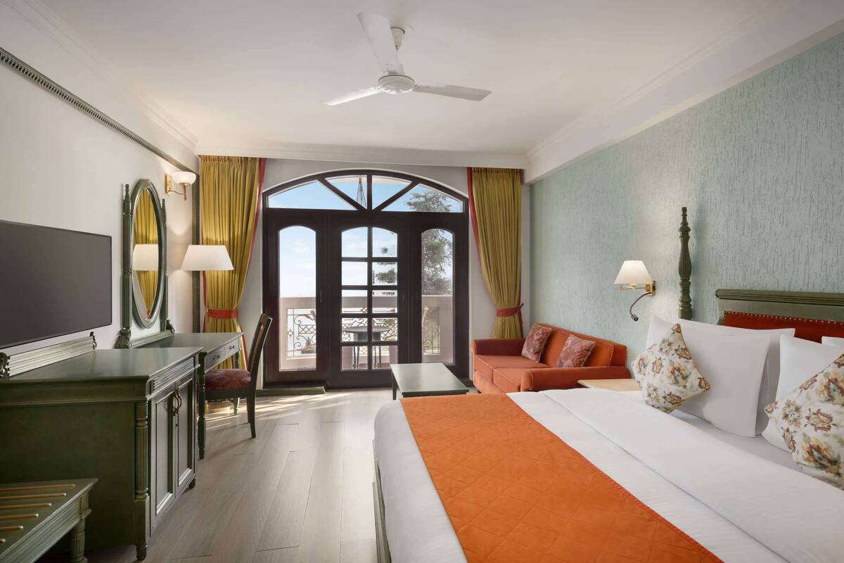 Une chambre d’hôtel comprenant un lit, un bureau, une chaise, un canapé, un balcon avec une table et une grande fenêtre.