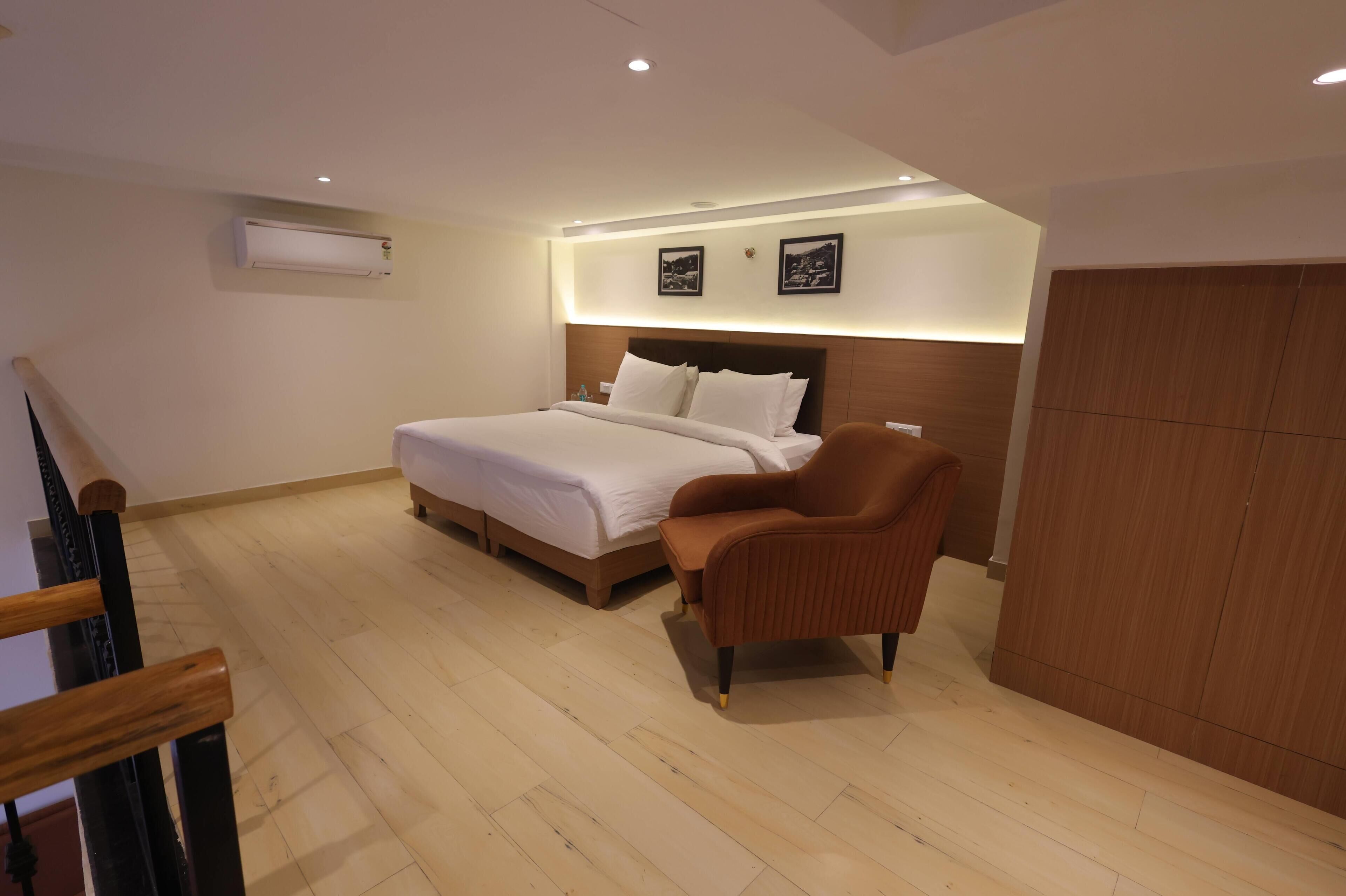 A modern hotel room with a large bed, a wooden wardrobe, and a brown armchair.