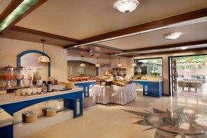 Enjoy a meal in our dining area with a buffet, round tables, and a view of lush greenery.