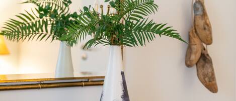 A wooden table with a white vase containing green foliage, a mirror with a gold frame, and a wall-mounted rope swing.