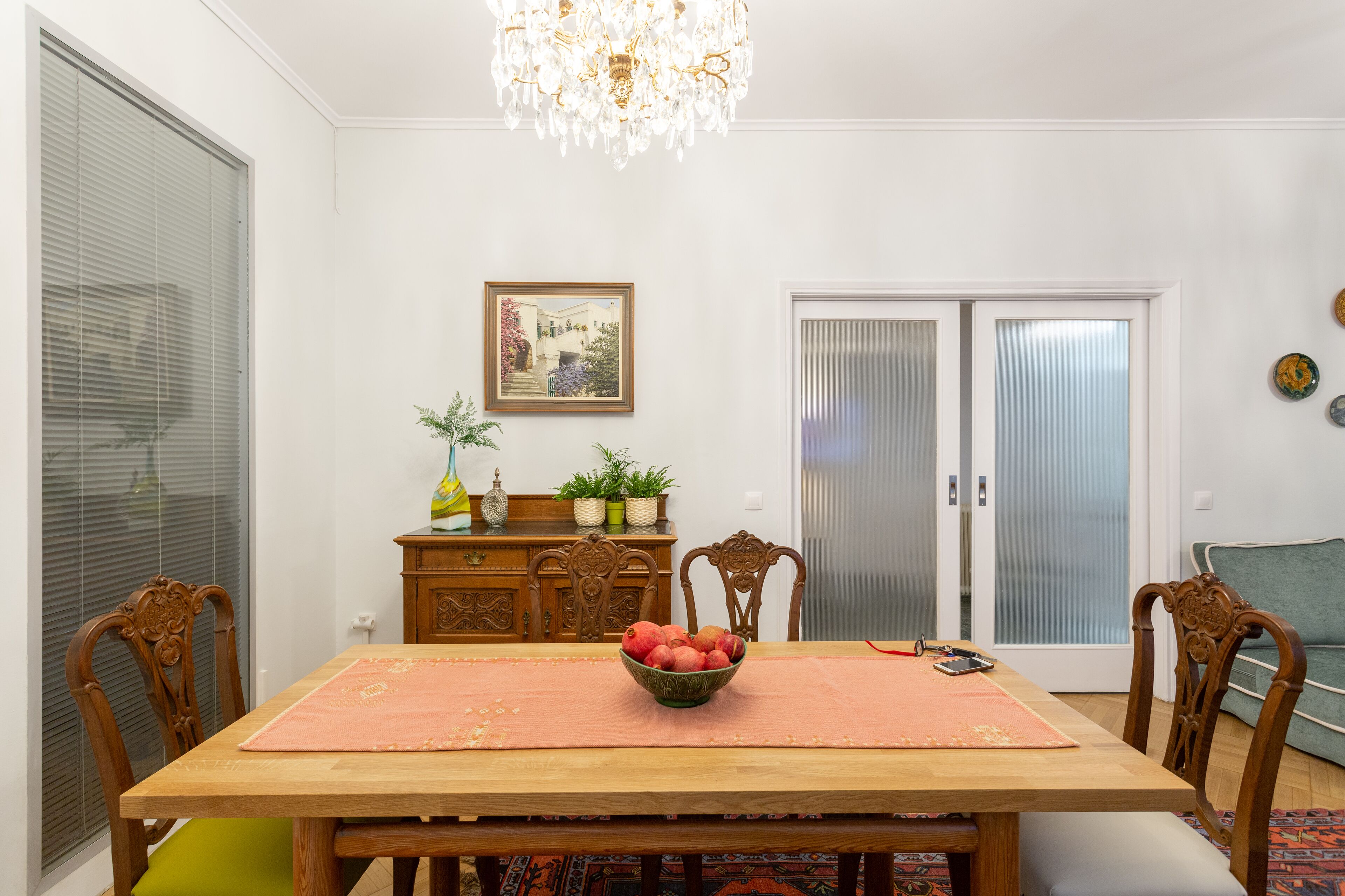 A dining area with a wooden table, chairs, a chandelier, a framed picture, and a sliding glass door.