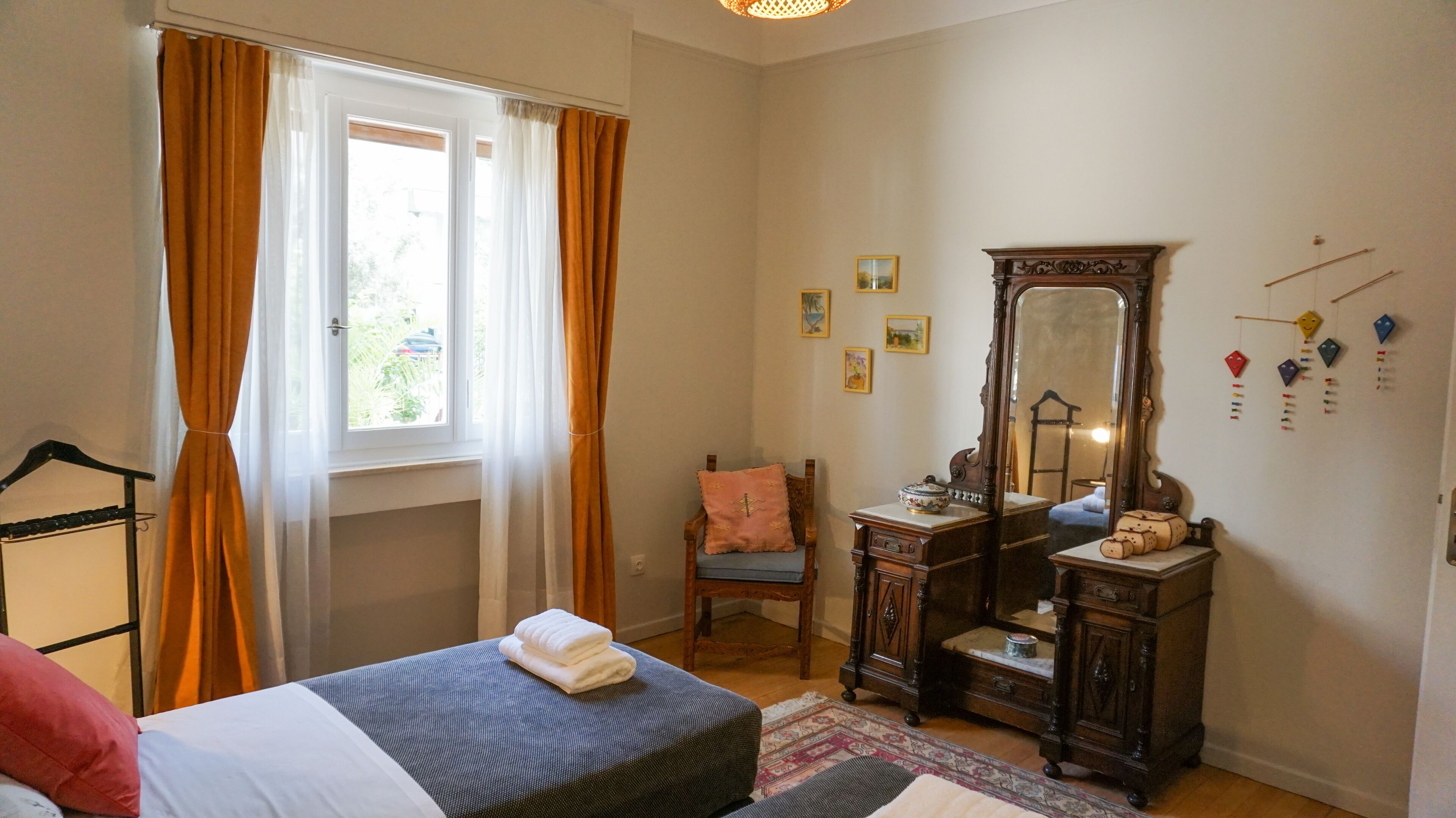 A bedroom with a bed, a dresser, a chair, a mirror, and a window with curtains.