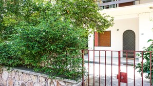 A stone wall with a metal gate, a building with a window and a door, and a tree in the foreground. - A Happy stay by Edem Beach (Palaio Faliro)