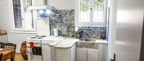 Una cocina compacta con armarios blancos, una estufa Bosch, un lavamanos y una ventana con persianas.