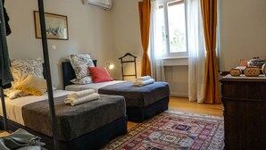 A room with two beds, a hanging rack, a patterned rug, and a window with curtains. - A Happy stay by Edem Beach (Palaio Faliro)