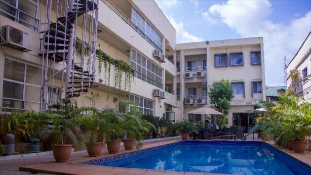 A pool area with potted plants and a building with multiple balconies. - Nne-Era Residence (Lagos)