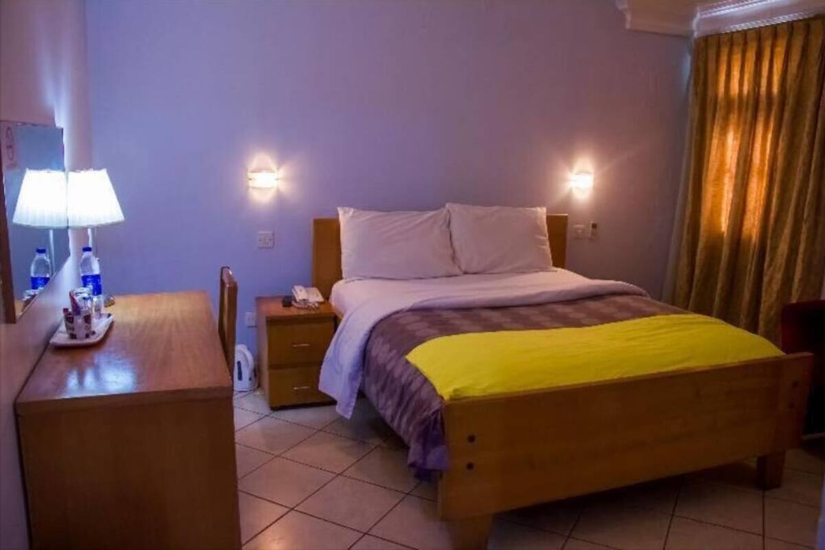 A hotel room with a bed, bedside table, lamp, and curtains.