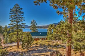 A cabin with a view of a lake and mountains, surrounded by pine trees.