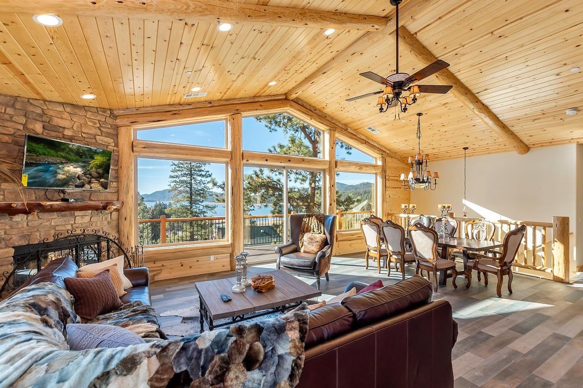 A spacious living area with a wooden ceiling, large windows, a fireplace, and a dining set.
