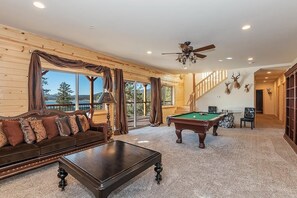 A spacious room with a pool table, a sofa, and a ceiling fan.
