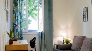 Een ruimtelijke woonkamer met een bank, een bureau, een stoel, een lamp en een raam met gordijnen.