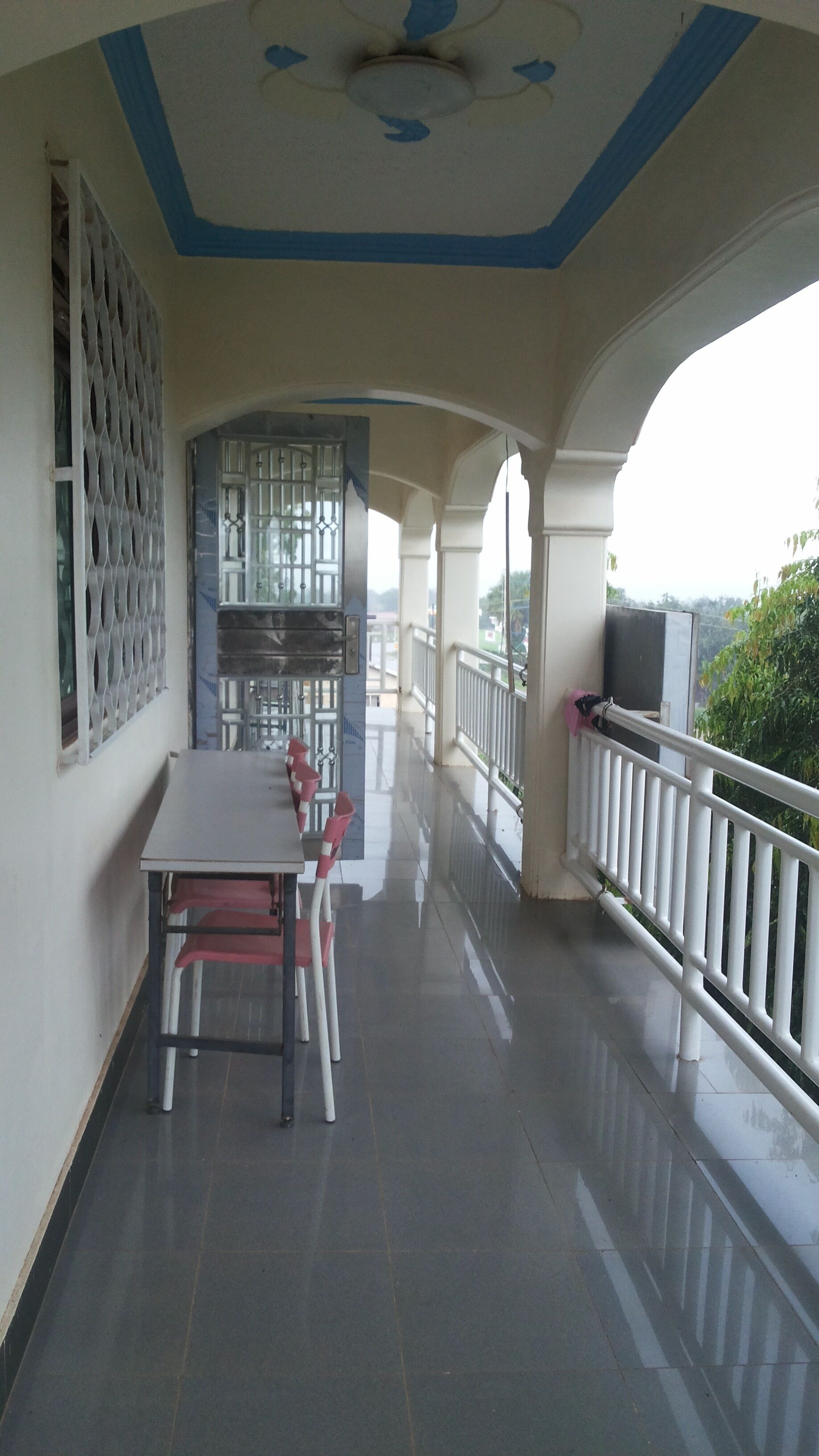 A covered balcony with a table and chairs, a decorative ceiling, and a view of greenery.