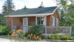 A small wooden cabin with a porch, surrounded by greenery and flowers. - Anchorage House & Cottages - Bayswater Cottage (Hubbards)