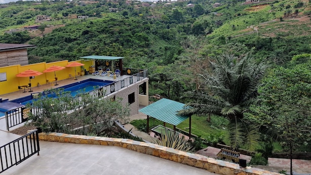 A pool area with yellow umbrellas, a stone wall, and a view of a lush green hillside.