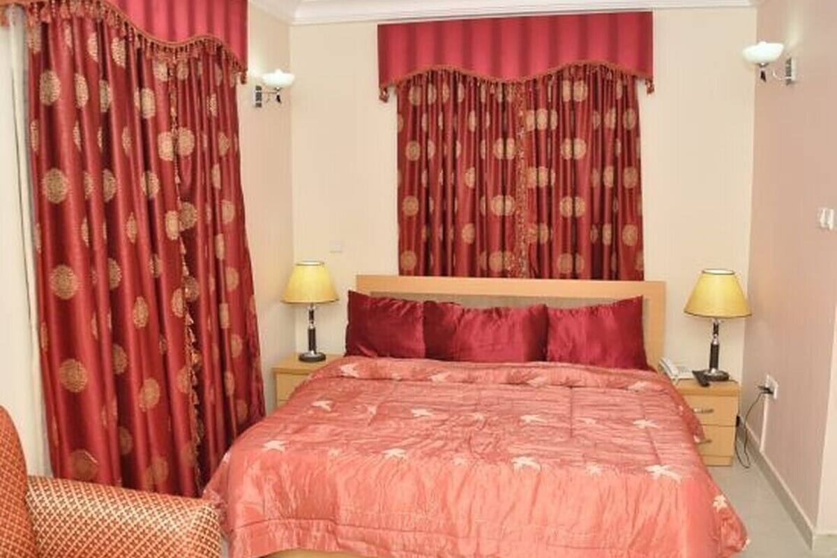 A bedroom with a large bed, two bedside tables with lamps, a wooden headboard, and red curtains with a circular pattern.