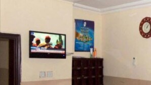Un área de recepción con un televisor montado en la pared, un reloj y un ventilador de pie.