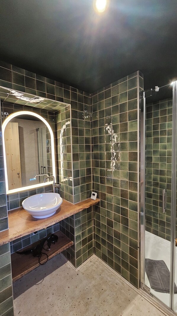 Un baño con un espejo grande, un lavamanos y una zona de ducha.