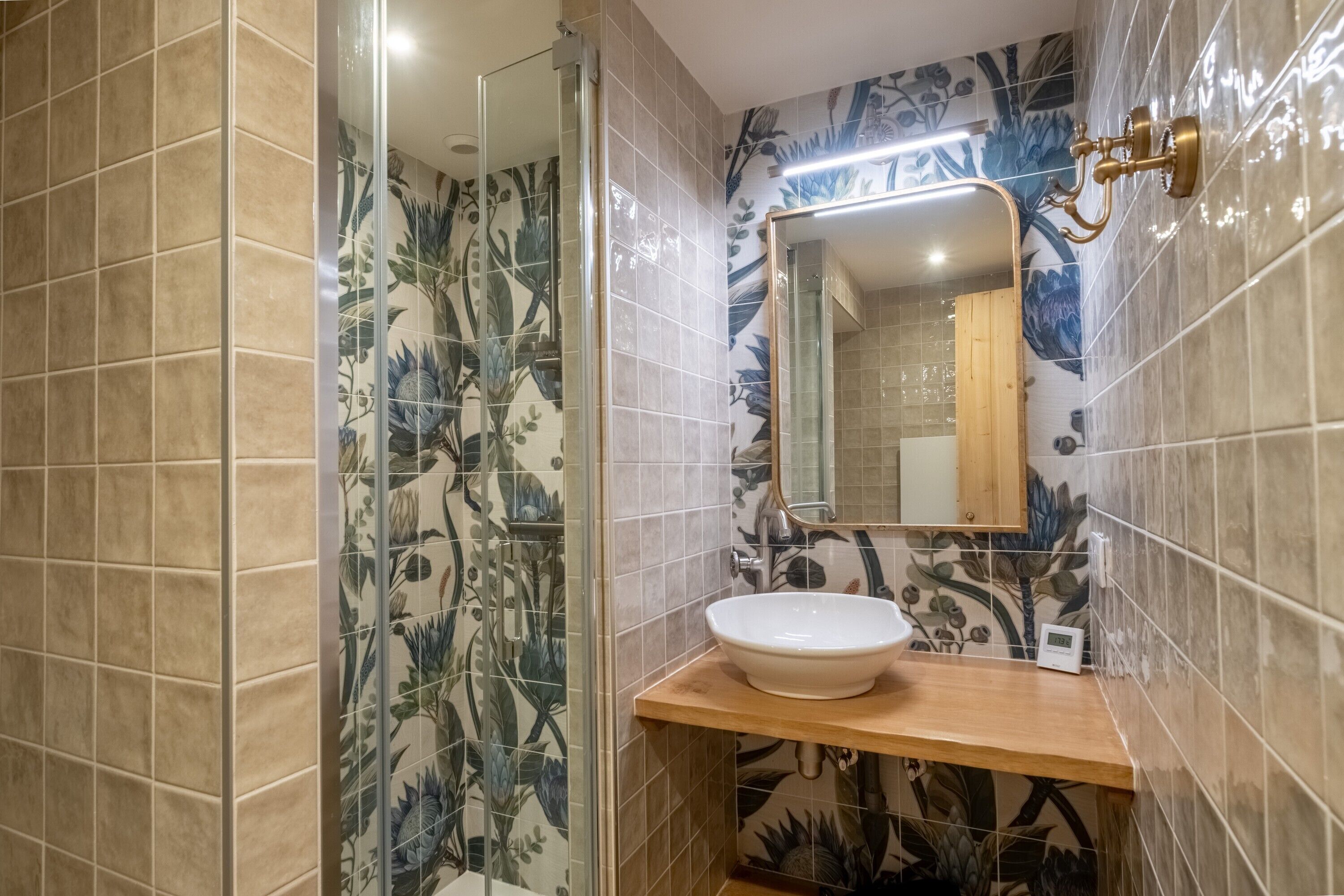 A bathroom with a white sink, a mirror, and floral-patterned tiles.
