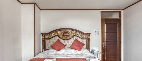 A neatly made bed with a wooden headboard, two red pillows, and a folded white towel on the bed.