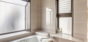 Ein modernes Badezimmer mit einer Badewanne, einem Fenster mit Metallgitter und einem Ablagefach für Pflegeutensilien.