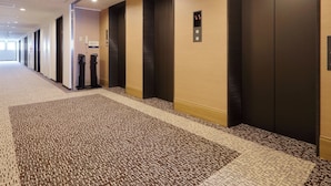A hotel corridor with carpeted flooring, multiple doors, and an elevator. - Keio Presso Inn Kanda (Tokyo)
