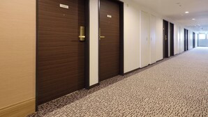 A hotel corridor with wooden doors numbered 1005 and 1006, carpeted flooring, and a plain wall. - Keio Presso Inn Kanda (Tokyo)