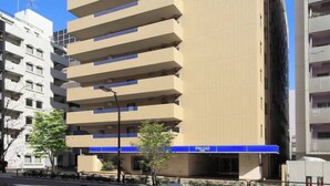 A tall, beige building with a blue sign on top and a blue awning at the bottom. - Keio Presso Inn Kanda (Tokyo)
