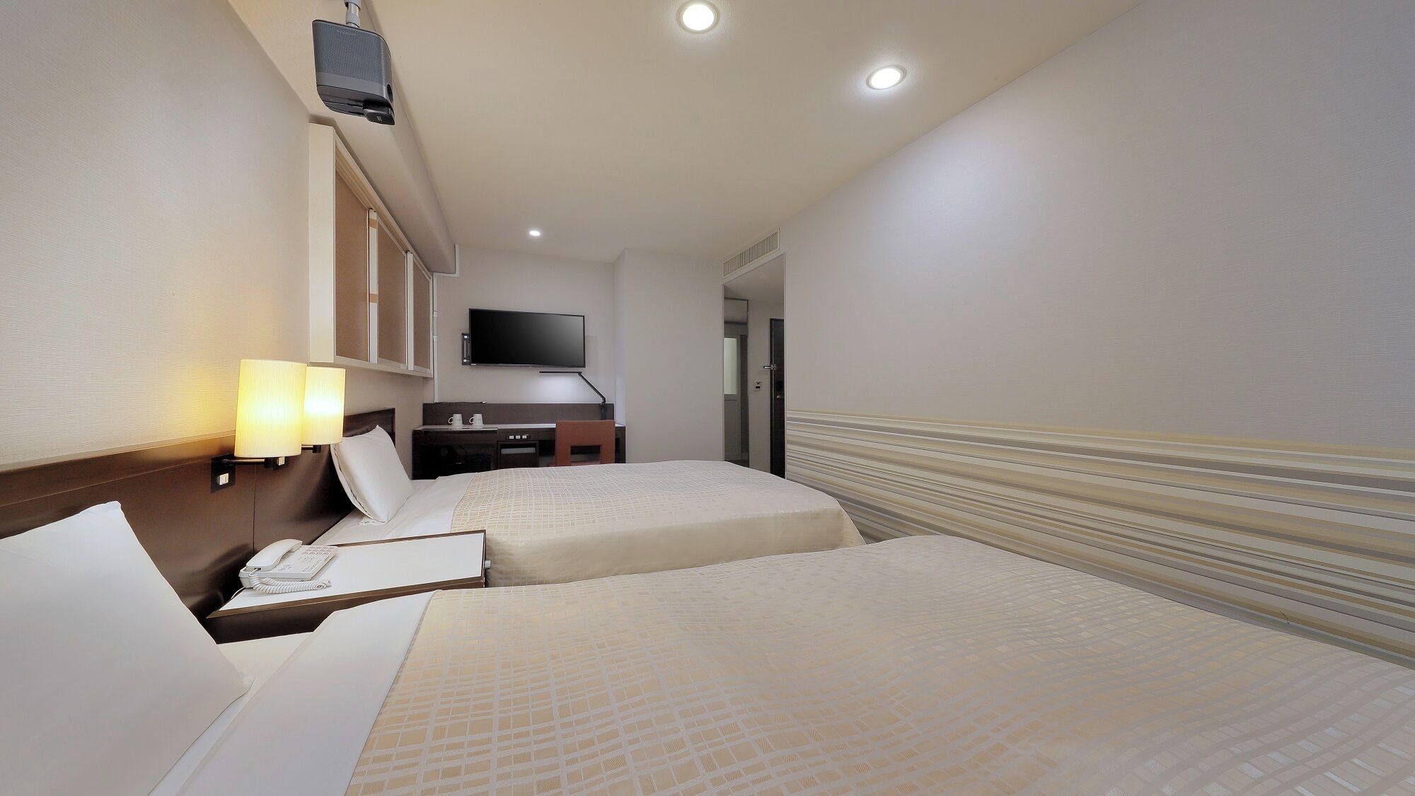 A hotel room with two beds, a desk with a telephone, a flat-screen TV, and a minibar.