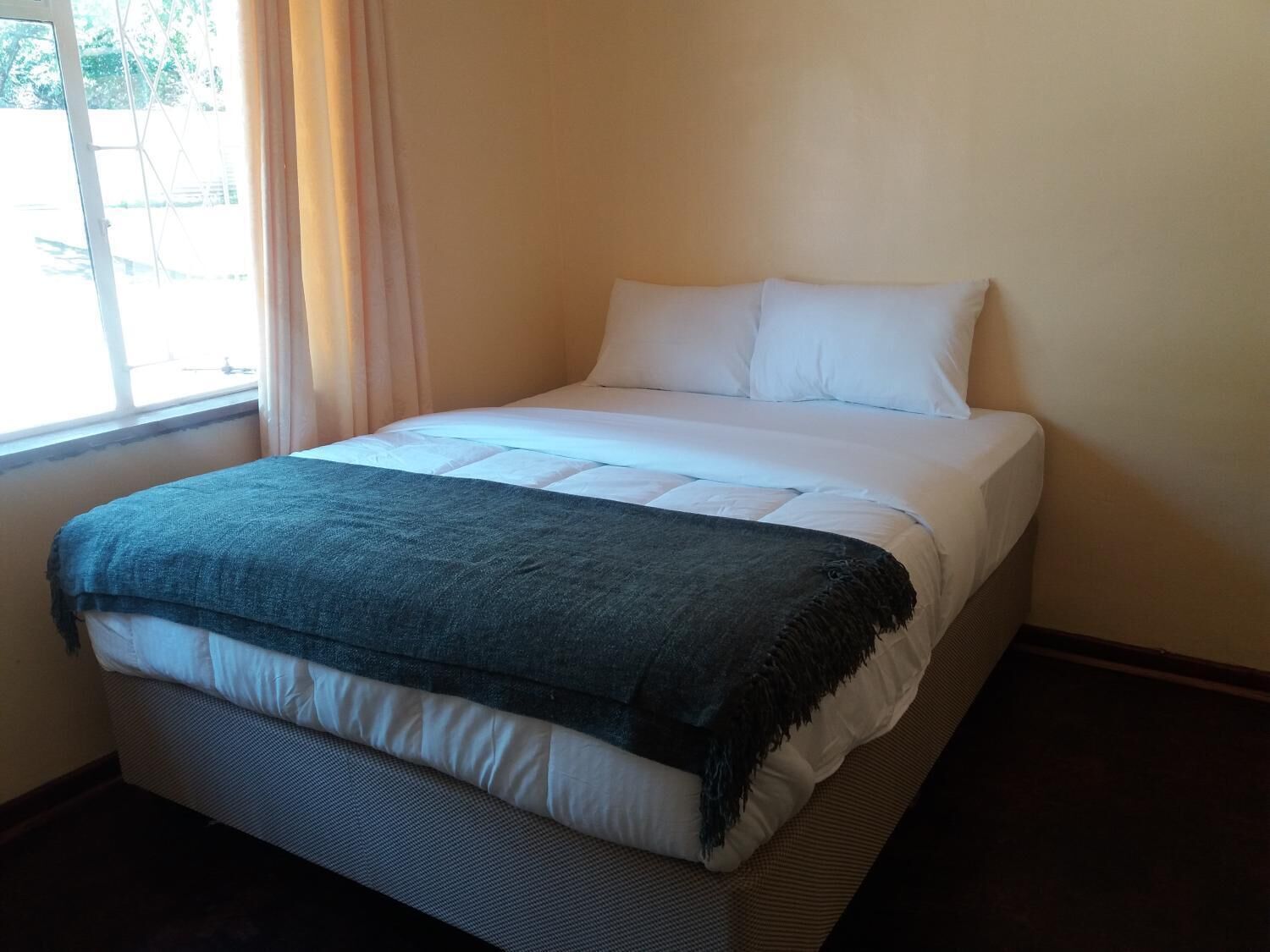 Una cama bien tendida con sábanas blancas y un plaid azul oscuro.