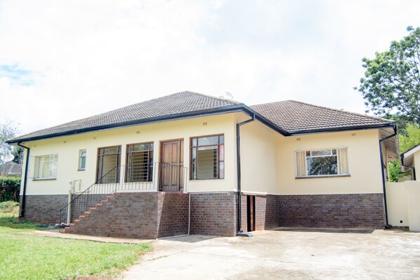 A two-story house with a brick foundation, a tiled roof, and a front porch. - Royal Guest House (Harare)