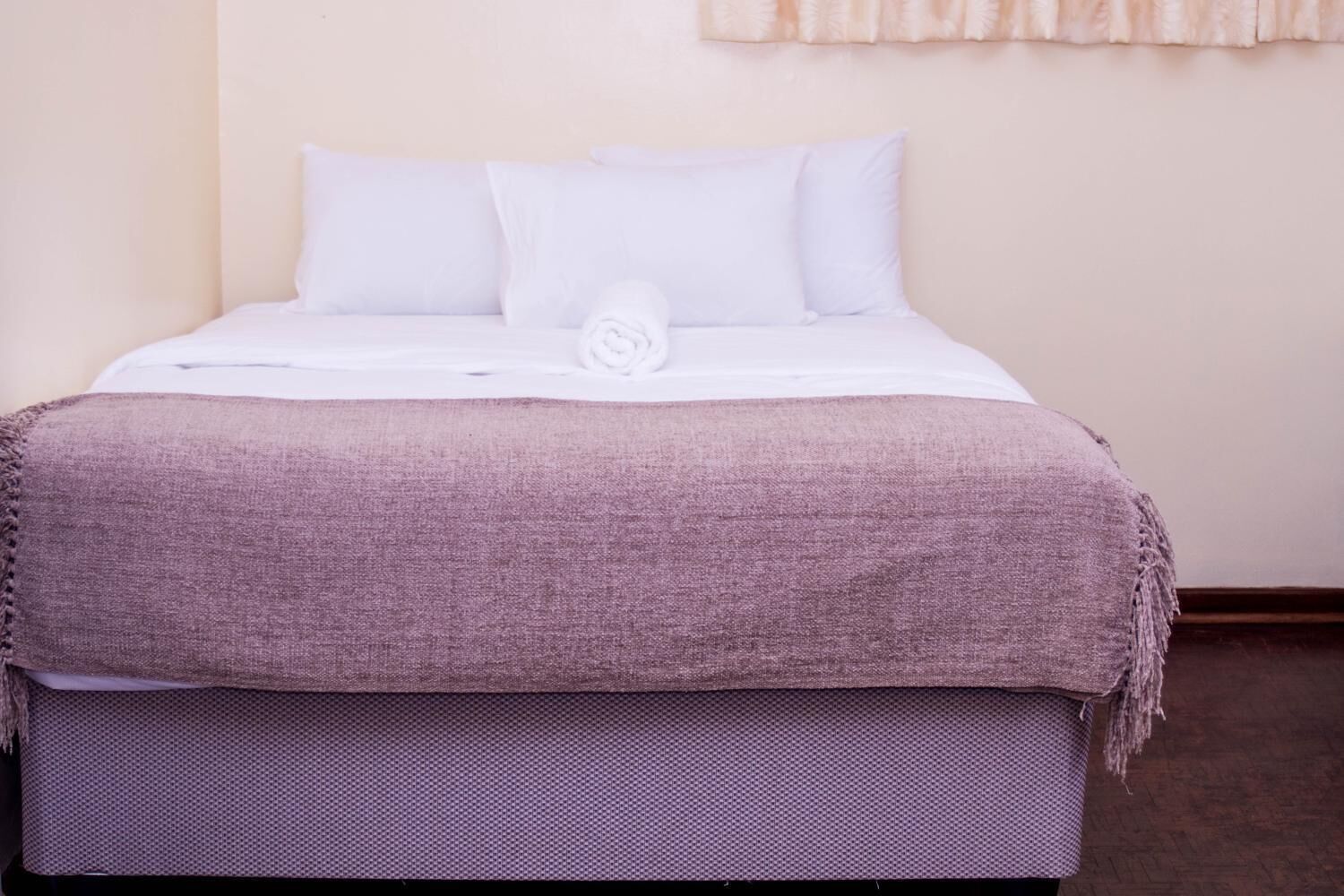 A neatly made bed with a white duvet and a purple blanket, a pillow, and a matching footboard.