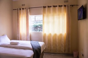 Un dormitorio con cama, cortinas, una ventana y televisor montado en la pared.