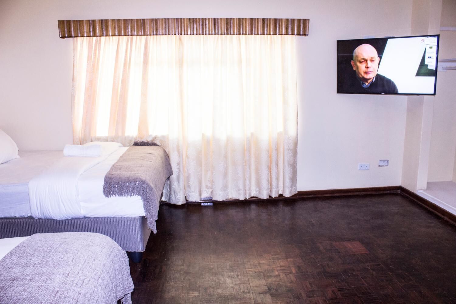 A hotel room with two beds, a television mounted on the wall, and a large window with curtains.