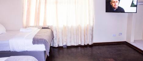 A hotel room with two beds, a television mounted on the wall, and a large window with curtains.