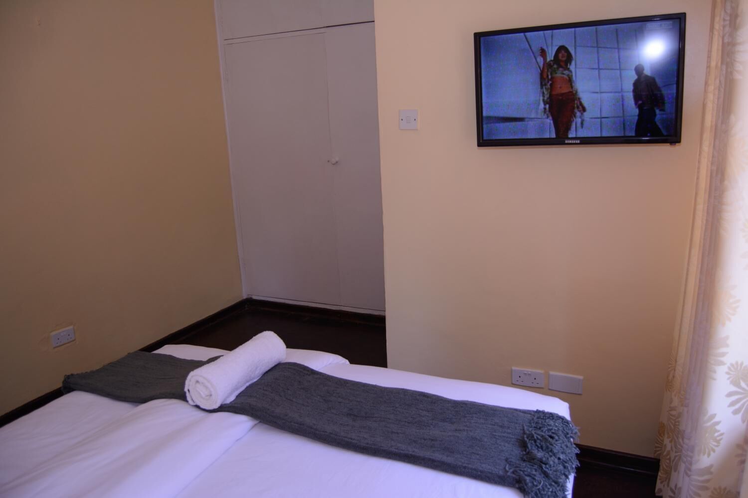 Una habitación de hotel con cama, televisión montada en la pared y armario.