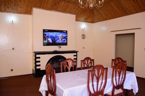 A dining room with a fireplace, wooden ceiling, and a television mounted on the wall. - Royal Guest House (Harare)