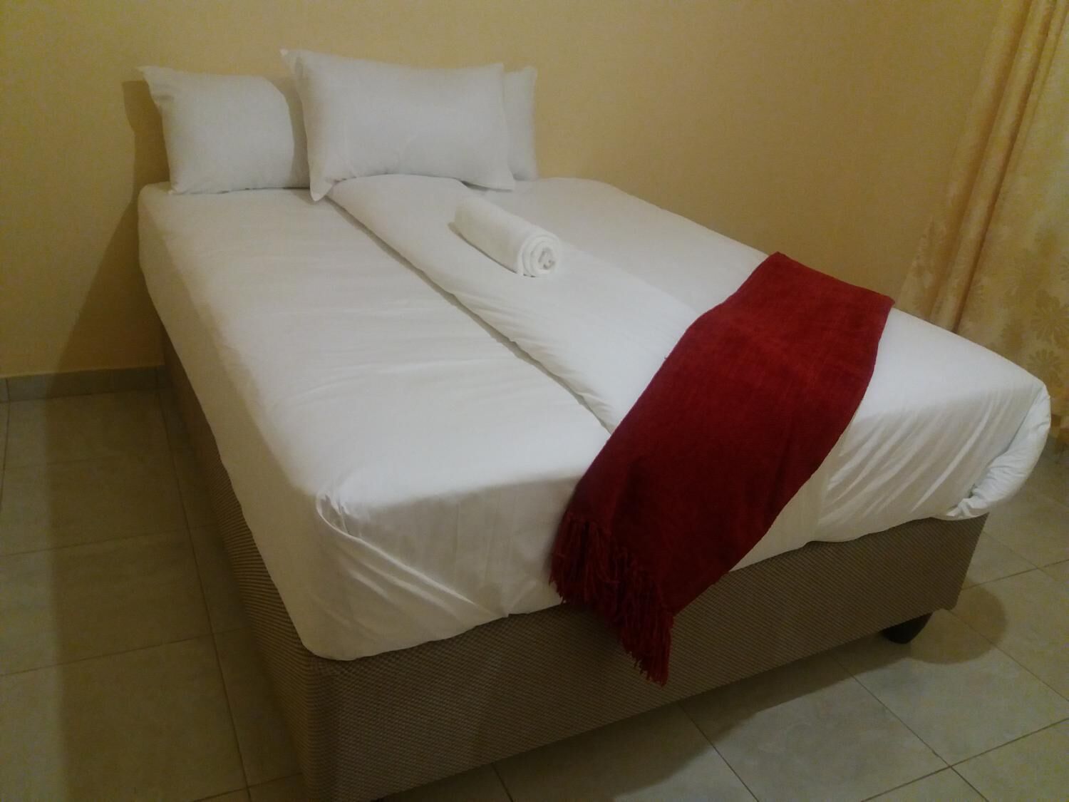 A bed with white bedding and a red throw blanket, a pillow, and a blanket on the side.