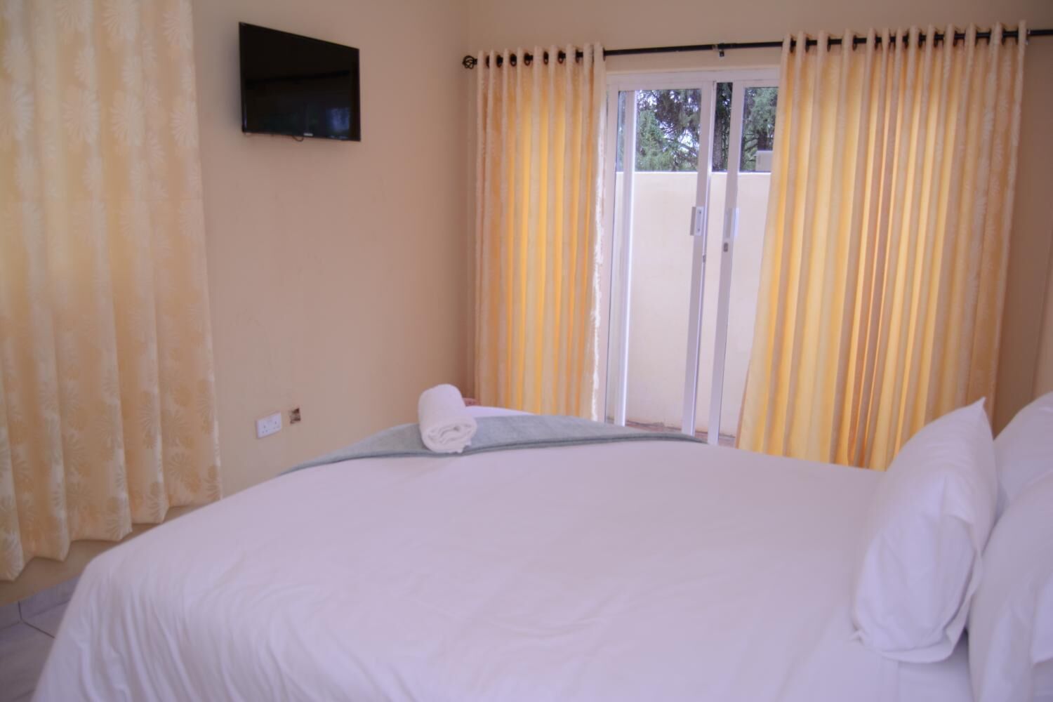 A hotel room with a bed, a television mounted on the wall, and a window with curtains.