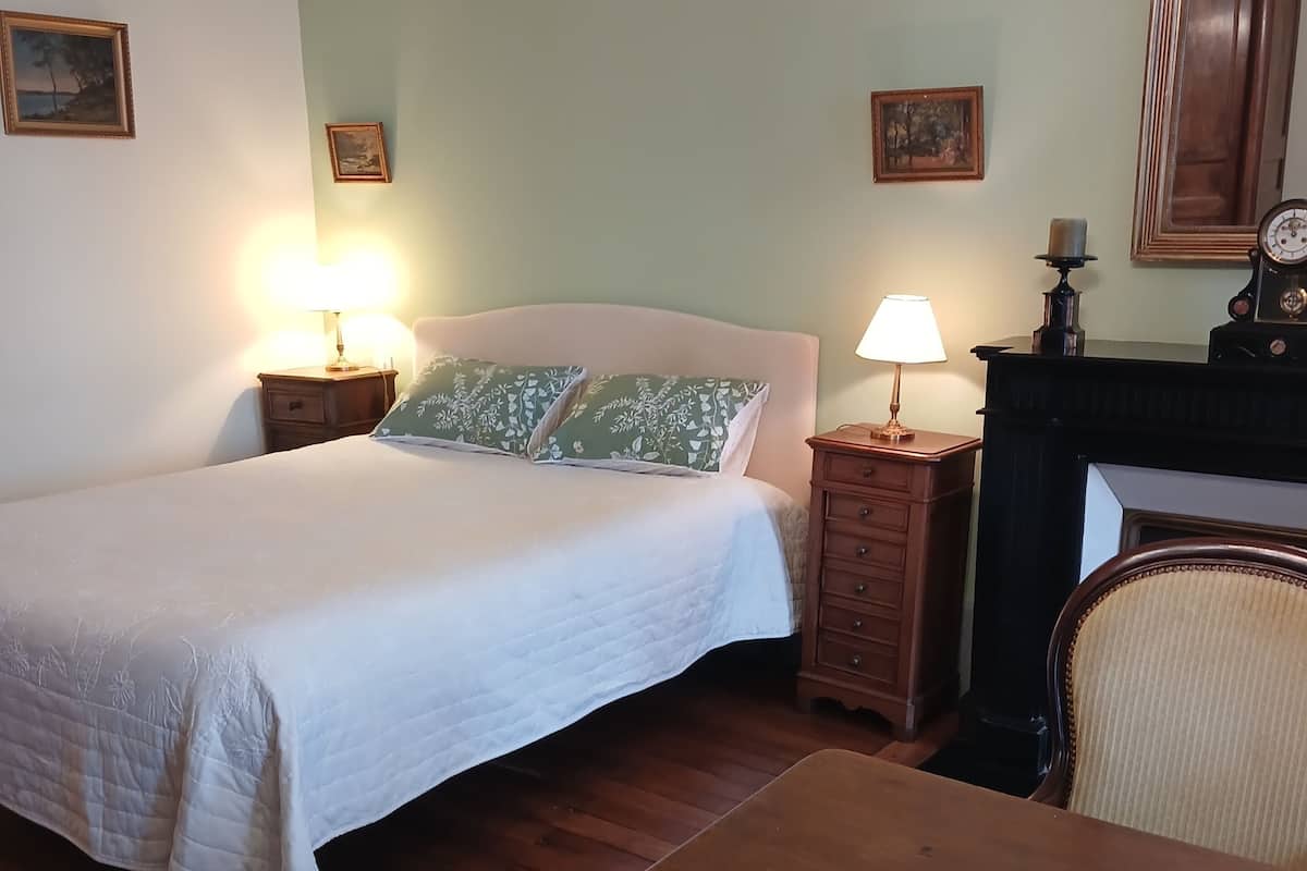 A bedroom with a bed, bedside tables, a chair, a table, and a fireplace.