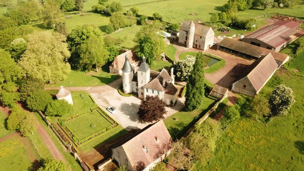 An aerial view of a historic estate with a central tower, surrounding buildings, and expansive green fields. - Chateau De Clusors (Saint-Menoux)