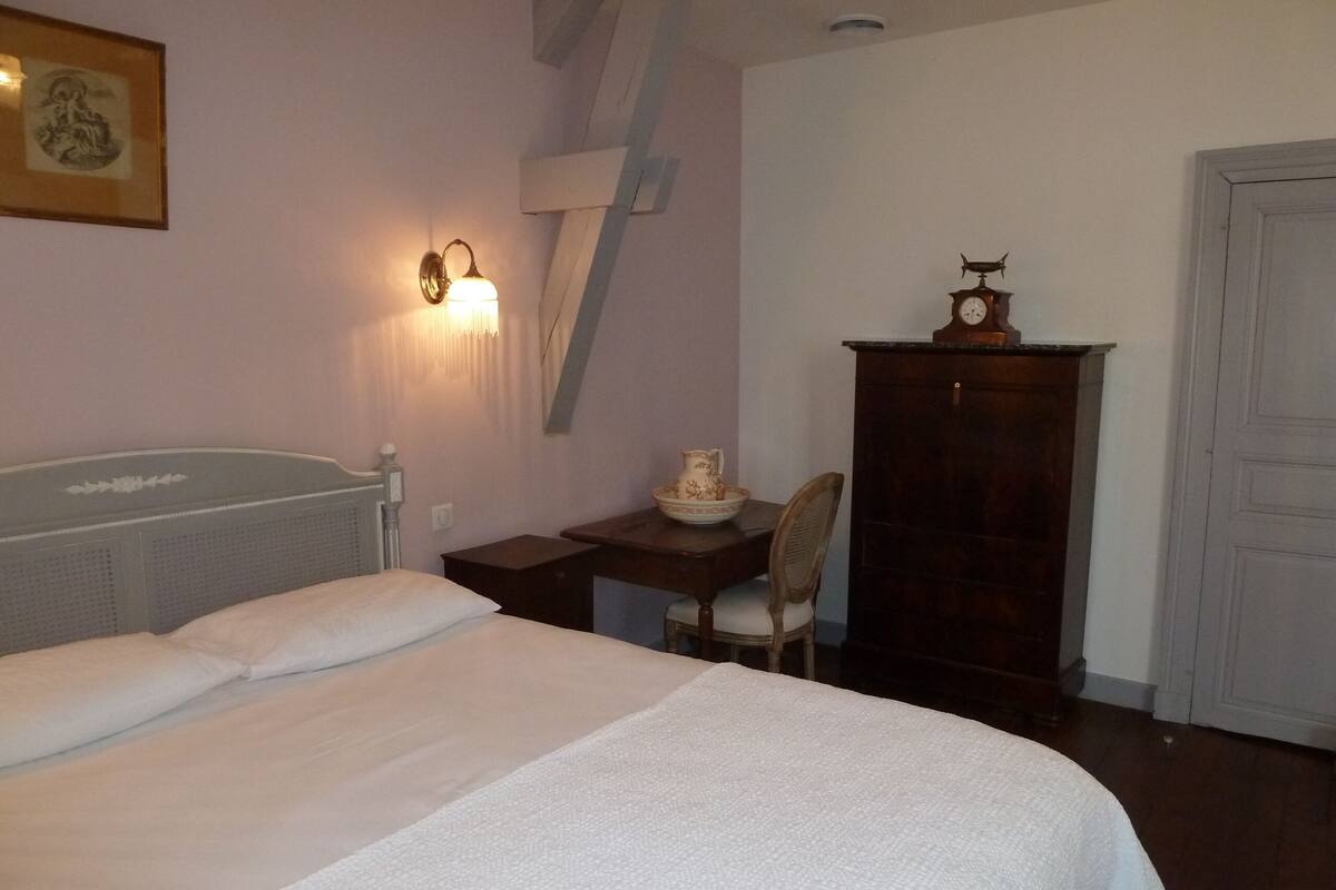 A bedroom with a bed, a desk, a chair, a clock, and a cabinet.