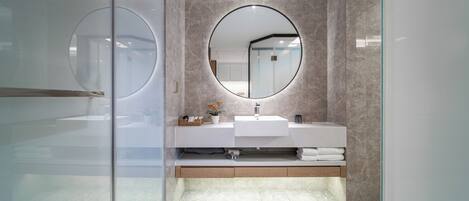 A modern bathroom with a glass shower enclosure, a round mirror, and a marble-tiled floor.